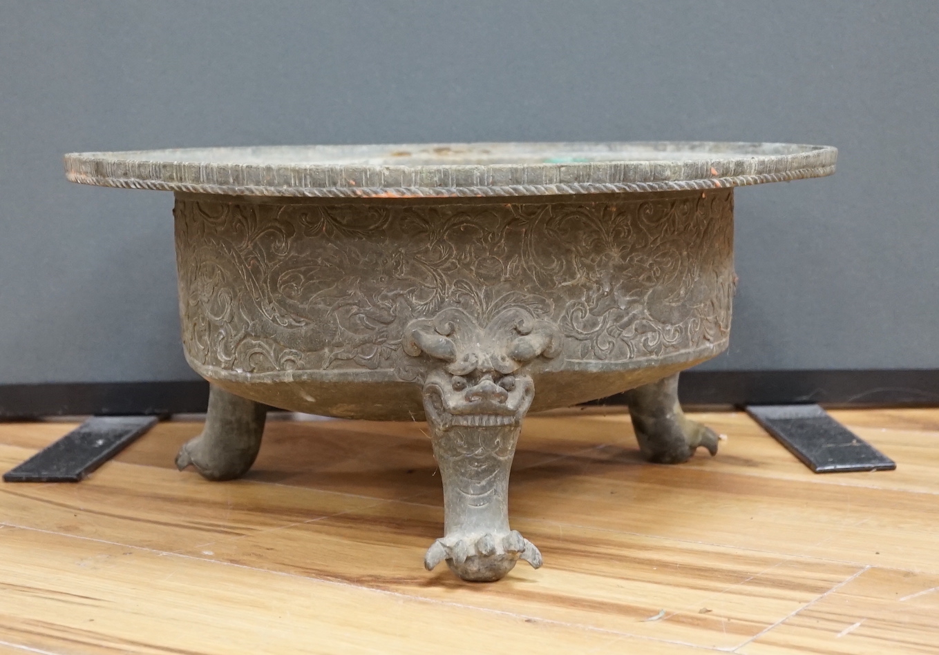 A large and heavy Chinese bronze tripod basin, Xuande mark but 19th century, the broad rim cast in relief with lions, brocaded balls and ribbons, the sides with dragons chasing flaming pearls, on three mythical beast hea